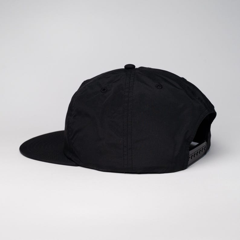 May include: A black, flat-brimmed baseball cap with a black adjustable strap in the back.