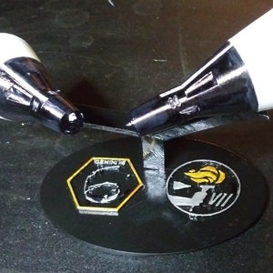May include: Two white and black model rockets on a black stand with a black and gold Gemini VIII patch and a black and gold patch with a flame and the number VIII.