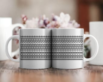 May include: Two white ceramic mugs with black stitch patterns on the front. The mugs have black handles and are sitting on a wooden table.