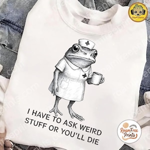 May include: White sweatshirt featuring a detailed black and white illustration of a frog dressed as a nurse, holding a mug. The text "I HAVE TO ASK WEIRD STUFF OR YOU'LL DIE" is printed below the frog.