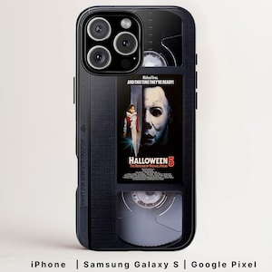 Puede incluir: Funda de teléfono negra con diseño de cinta VHS, que muestra el cartel de la película "Halloween 5: The Revenge of Michael Myers". La funda incluye el texto "Michael lives. AND THIS TIME THEY'RE READY!" y es compatible con iPhone, Samsung Galaxy S y Google Pixel.