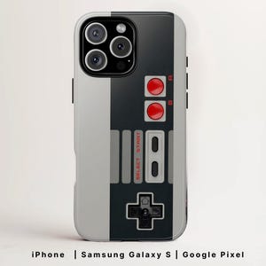 May include: A phone case featuring a retro video game controller design. The case is split vertically, with a light gray side and a black side. The black side has red buttons, a directional pad, and the text "SELECT START".