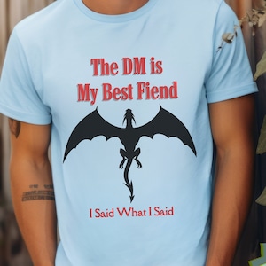 May include: Light blue t-shirt with a black dragon silhouette and the text "The DM is My Best Fiend I Said What I Said".