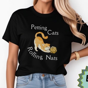 May include: A black t-shirt with a white graphic of a cat playing with a dice. The text on the shirt reads "Petting Cats Rolling Nats".