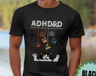 May include: Black t-shirt with the text "ADHD&D" in white with a graphic of a black and white cat with yellow eyes and a string of colorful dice hanging above the cat.