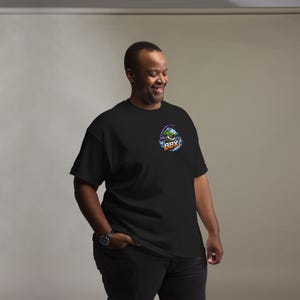 Puede incluir: Una camiseta negra de manga corta con un pequeño gráfico en el pecho izquierdo. El gráfico muestra un pez de dibujos animados verde con una caña de pescar, rodeado de salpicaduras de agua azul y el texto BBX en naranja y blanco debajo.