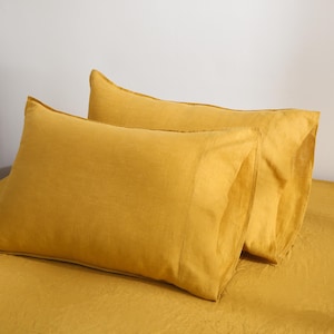May include: Two mustard yellow linen pillowcases. The pillowcases are made from a soft, natural fabric and have a subtle texture.