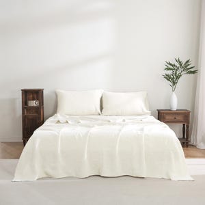May include: A white linen bedding set with a crisp, wrinkle-free finish. The set includes a flat sheet, fitted sheet, and two pillowcases. The bedding is displayed on a bed with a wooden headboard and side tables.