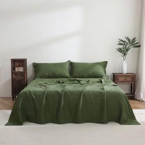 Puede incluir: Un edred&oacute;n de lino verde con dos fundas de almohada a juego. El edred&oacute;n est&aacute; doblado hacia atr&aacute;s para revelar las s&aacute;banas de lino verde debajo. La cama est&aacute; en un dormitorio con una mesita de noche de madera y un jarr&oacute;n con plantas verdes.