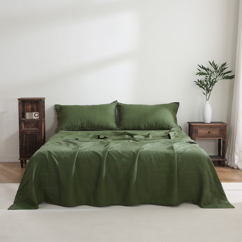 Puede incluir: Un edred&oacute;n de lino verde con dos fundas de almohada a juego. El edred&oacute;n est&aacute; doblado hacia atr&aacute;s para revelar las s&aacute;banas de lino verde debajo. La cama est&aacute; en un dormitorio con una mesita de noche de madera y un jarr&oacute;n con plantas verdes.