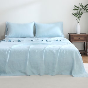 May include: A light blue linen bed sheet set with two matching pillowcases. The sheet is smooth and wrinkle-free, with a subtle sheen.