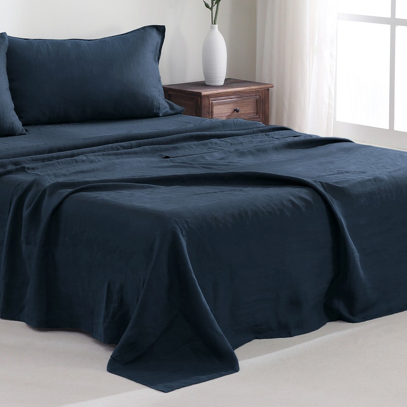 Puede incluir: Una s&aacute;bana de cama de lino azul oscuro con una funda de almohada a juego. La s&aacute;bana est&aacute; doblada y drapeada sobre un marco de cama.