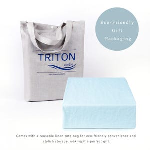 Puede incluir: Una bolsa de lona de lino azul claro con el texto "TRITON LINEN 100% FRENCH LINEN" impreso en ella. La bolsa est&aacute; sentada sobre una tela de lino azul claro. El texto "Eco-Friendly Gift Packaging" est&aacute; escrito en un c&iacute;rculo sobre la bolsa.