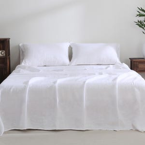 May include: A white linen bed sheet and two white linen pillowcases on a bed with a white headboard.