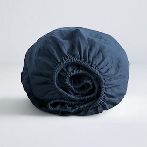 May include: A deep blue fitted sheet made of linen, rolled up and ready to be used on a bed.