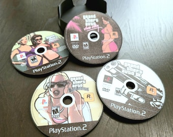 May include: Four circular PlayStation 2 game discs featuring Grand Theft Auto titles including Vice City, San Andreas, and Grand Theft Auto III. Each disc displays the PlayStation 2 logo, the ESRB M rating, and specific character or weapon artwork.