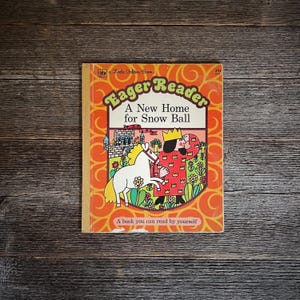 May include: A vintage orange and yellow children's book titled "Eager Reader: A New Home for Snow Ball". The cover features a cartoon illustration of a king and a white horse.