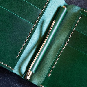 May include: A green leather wallet with a pen holder. The wallet has multiple card slots and a stitched edge.