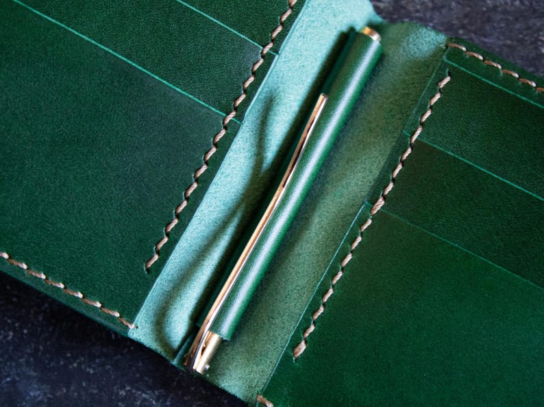May include: A green leather wallet with a pen holder. The wallet has multiple card slots and a stitched edge.