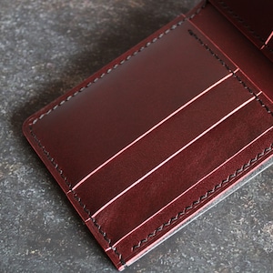 May include: A burgundy leather wallet with multiple card slots and a billfold. The wallet has black stitching around the edges.