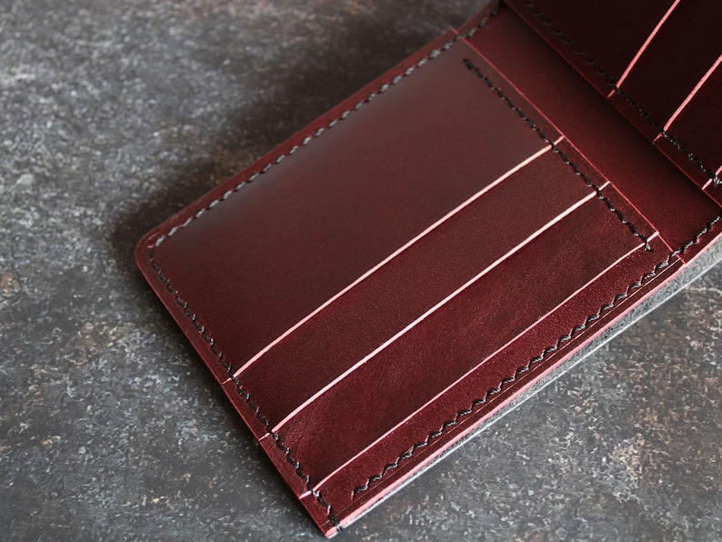 May include: A burgundy leather wallet with multiple card slots and a billfold. The wallet has black stitching around the edges.