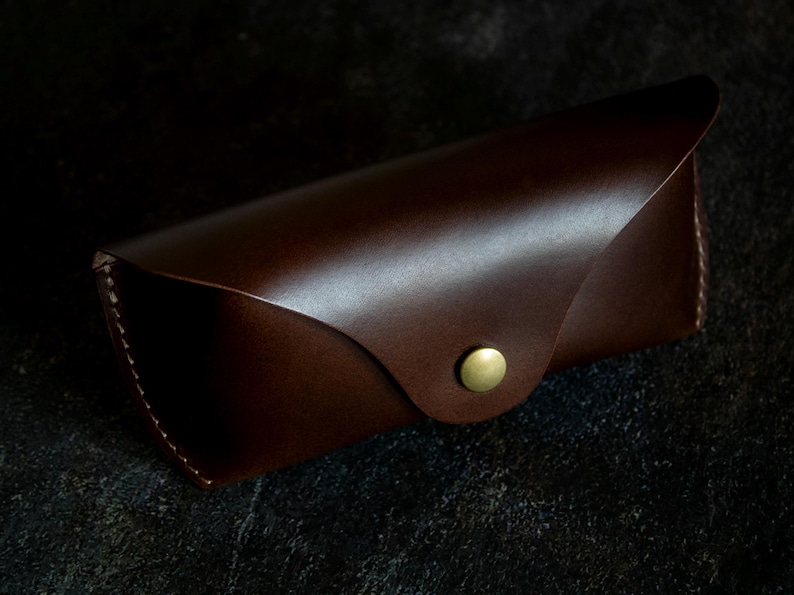 May include: A brown leather glasses case with a gold button closure.