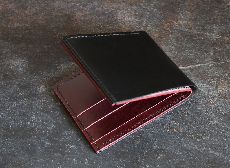May include: A black leather wallet with a burgundy leather interior. The wallet is folded in half and the interior is visible.