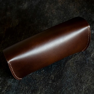 May include: A brown leather case with a stitched edge.