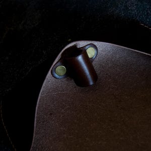 May include: Close-up of the inside of a brown leather bag with a brown leather strap loop and two brass snaps.