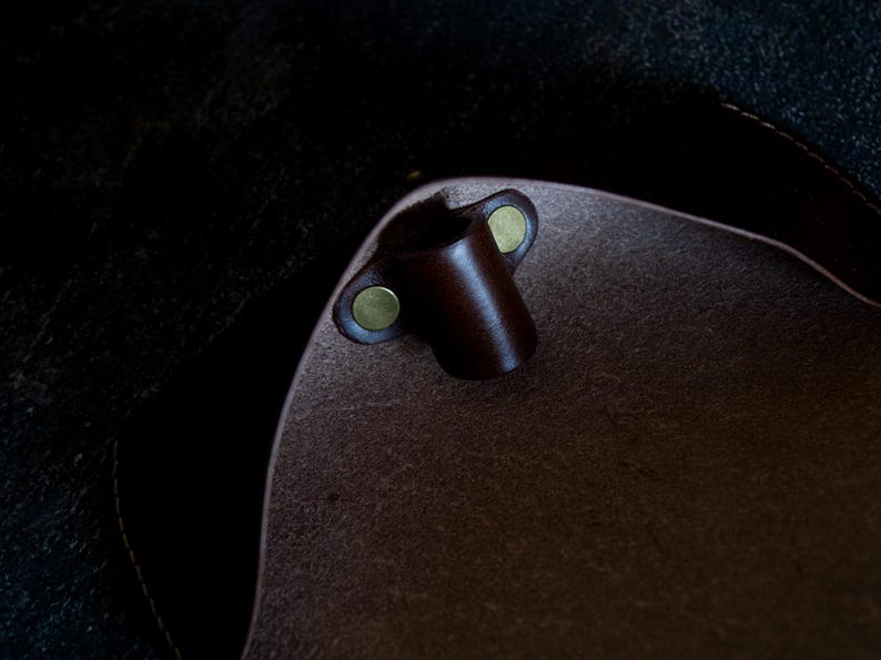 May include: Close-up of the inside of a brown leather bag with a brown leather strap loop and two brass snaps.