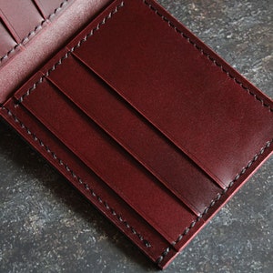 May include: A burgundy leather wallet with black stitching and multiple card slots.