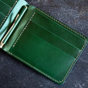 May include: A green leather wallet with a money clip and multiple card slots. The wallet has a stitched edge.