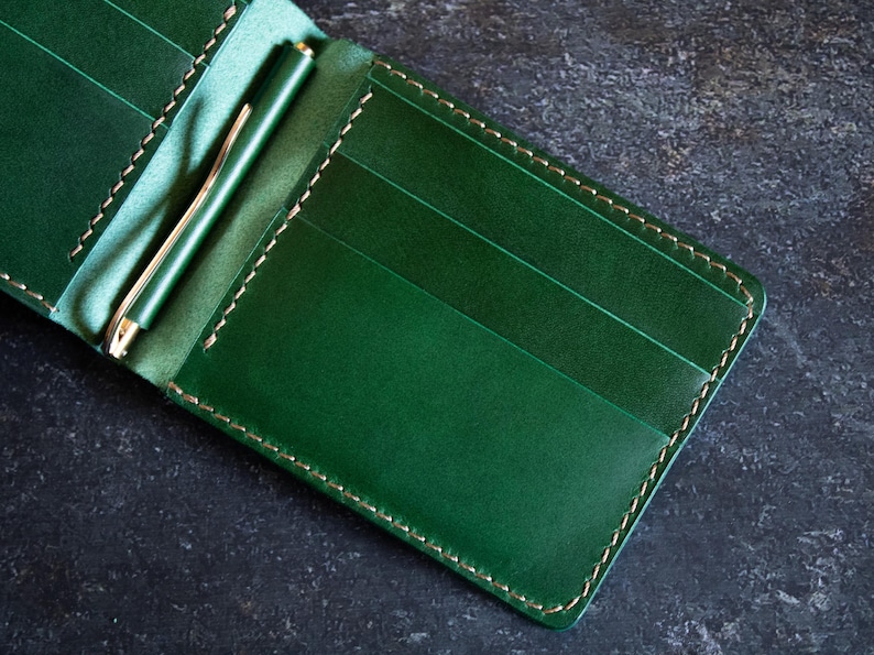 May include: A green leather wallet with a money clip and multiple card slots. The wallet has a stitched edge.