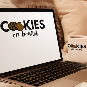 Puede incluir: Un ordenador portátil con una pantalla blanca que muestra el texto "COOKIES on board" con un gráfico de dos galletas. Una taza de café blanca con el mismo texto y gráfico está sentada en el portátil. El portátil y la taza están en una cama con una manta.