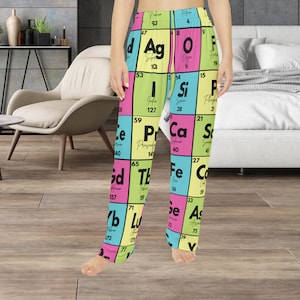 Puede incluir: Un pantalón de pijama amarillo, rosa y azul con un patrón de la tabla periódica de los elementos. El pantalón tiene una cintura elástica negra y un cordón de ajuste negro.