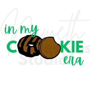 Puede incluir: Texto verde que dice "in my cookie era" con una galleta marrón partida por la mitad. La galleta es una galleta tradicional Girl Scout Thin Mint.