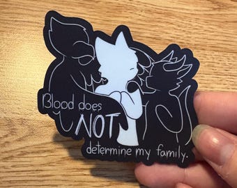 May include: A black and white sticker with three animal figures. A white figure is in the centre, with two black figures on either side. The text "Blood does NOT determine my family" is written on the sticker.