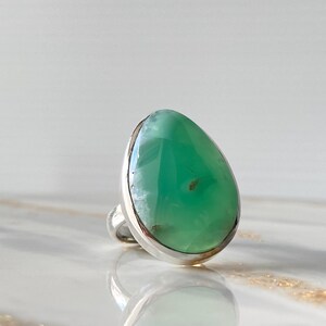 May include: A teardrop-shaped green gemstone ring set in sterling silver. The ring features a unique, natural green gemstone with a smooth, polished surface.