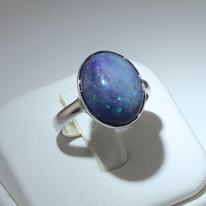 May include: A silver ring featuring a large, oval-shaped opal. The opal displays a dark blue base color with vibrant flashes of green, red, and blue. The ring's band is a simple, polished silver.