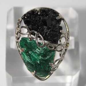May include: A silver ring with a black and green gemstone setting. The ring is designed with a delicate, intricate pattern.