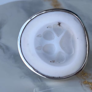 May include: A white ceramic ring with a silver band featuring a paw print design.