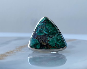 Könnte beinhalten: Ein dreieckiger Ring mit einem grünen und braunen Edelstein, der in eine silberne Fassung gefasst ist.