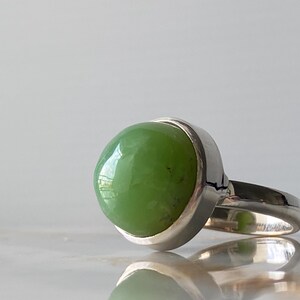 May include: A silver ring with a green gemstone set in a bezel setting.