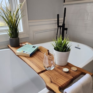 Peut inclure: Un plateau de bain en bois avec un livre, un verre et deux bougies. Le plateau est placé sur le bord d'une baignoire blanche. Une serviette blanche est suspendue au plateau.