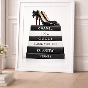 May include: A framed print showing black high-heeled shoes with red soles and bows, placed on a stack of books. The books are black and white, with designer names such as Chanel, Dior, and Gucci on their spines. The artwork is set against a white backdrop.