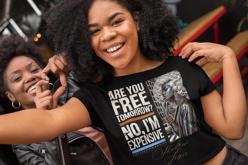 May include: Black t-shirt with the text "ARE YOU FREE TOMORROW? NO, I'M EXPENSIVE" and an illustration of a woman with silver hair. The shirt is worn by a person smiling.