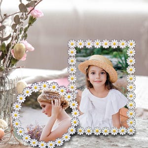 Puede incluir: Dos marcos de fotos con bordes de flores de margarita. Uno es ovalado, el otro rectangular. Los marcos contienen imágenes de una mujer y una niña. Un jarrón de flores y huevos de Pascua están en el fondo.