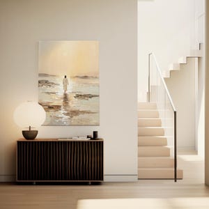 Peut inclure: Une peinture à l'huile représente une figure marchant sur l'eau vers une lumière vive. L'œuvre est accrochée au-dessus d'un meuble en bois foncé avec une lampe ronde. Un escalier avec une rampe blanche est visible.