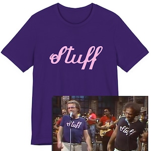 May include: A purple t-shirt featuring the word "Stuff" in a light pink, cursive script. The image also includes a smaller image of a band wearing similar t-shirts with the same text.