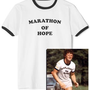 May include: White t-shirt with black trim displaying the words "MARATHON OF HOPE" in black. The image includes a smaller photo of a person wearing a similar shirt while running. The shirt has a classic, athletic design.